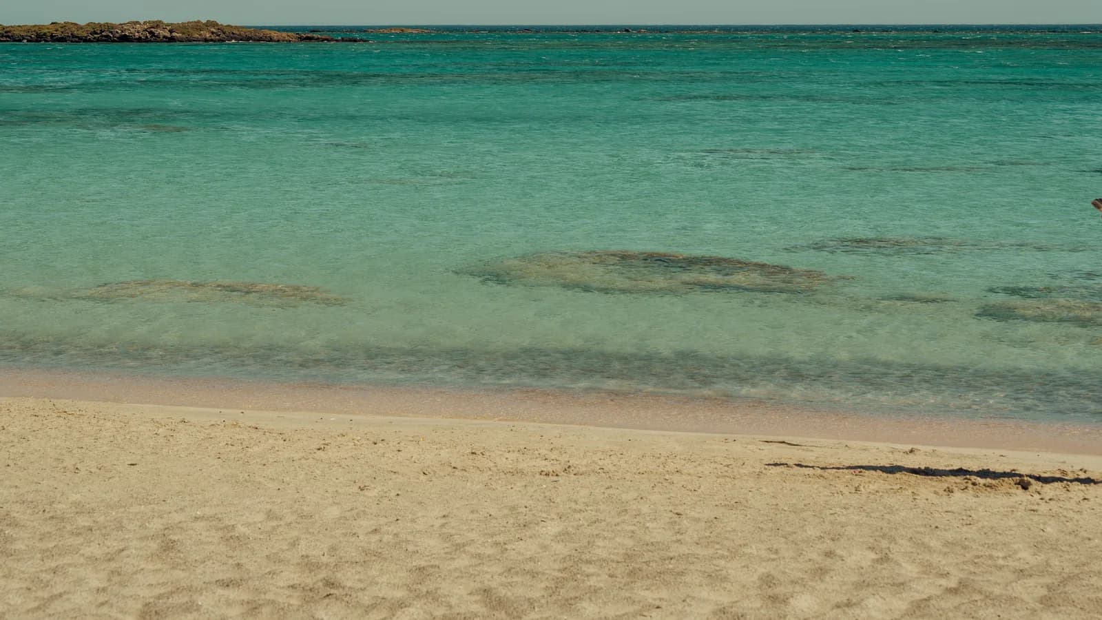 Plage de sable clair et mer calme turquoise sur la côte est de Chypre, un îlot rocheux à l'horizon