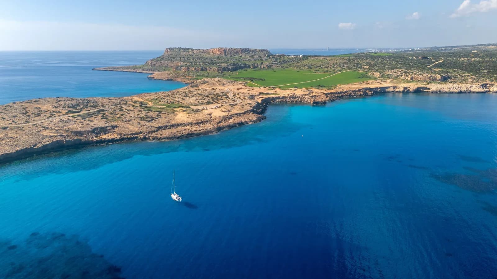 Vue aérienne du cap Greco : péninsule rocheuse, mer d'un bleu profond et voilier à l'ancre