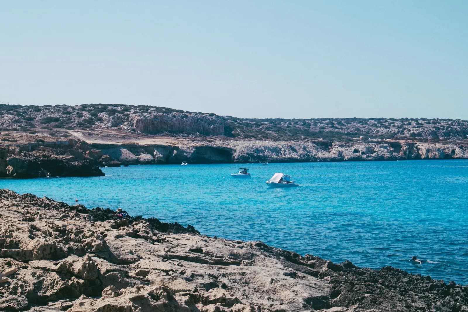 Eau turquoise et bateaux d'excursion ancrés le long d'une côte rocheuse sauvage à Chypre