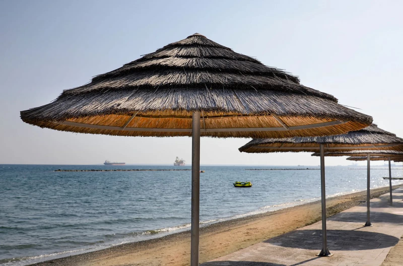Plage de Limassol, à Chypre, presque déserte en hiver : parasols de paille, mer calme et cargos à l'horizon sous un ciel pâle