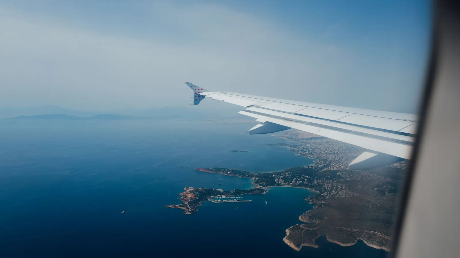 Aile d'un avion de ligne vue depuis le hublot, en approche d'une côte et d'îlots en Méditerranée