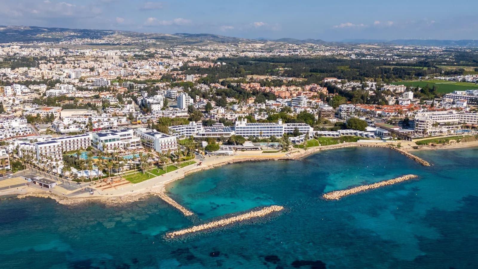 Vue aérienne d'une côte méditerranéenne de Chypre : plage, hôtels et immeubles blancs, brise-lames en pierre et mer turquoise