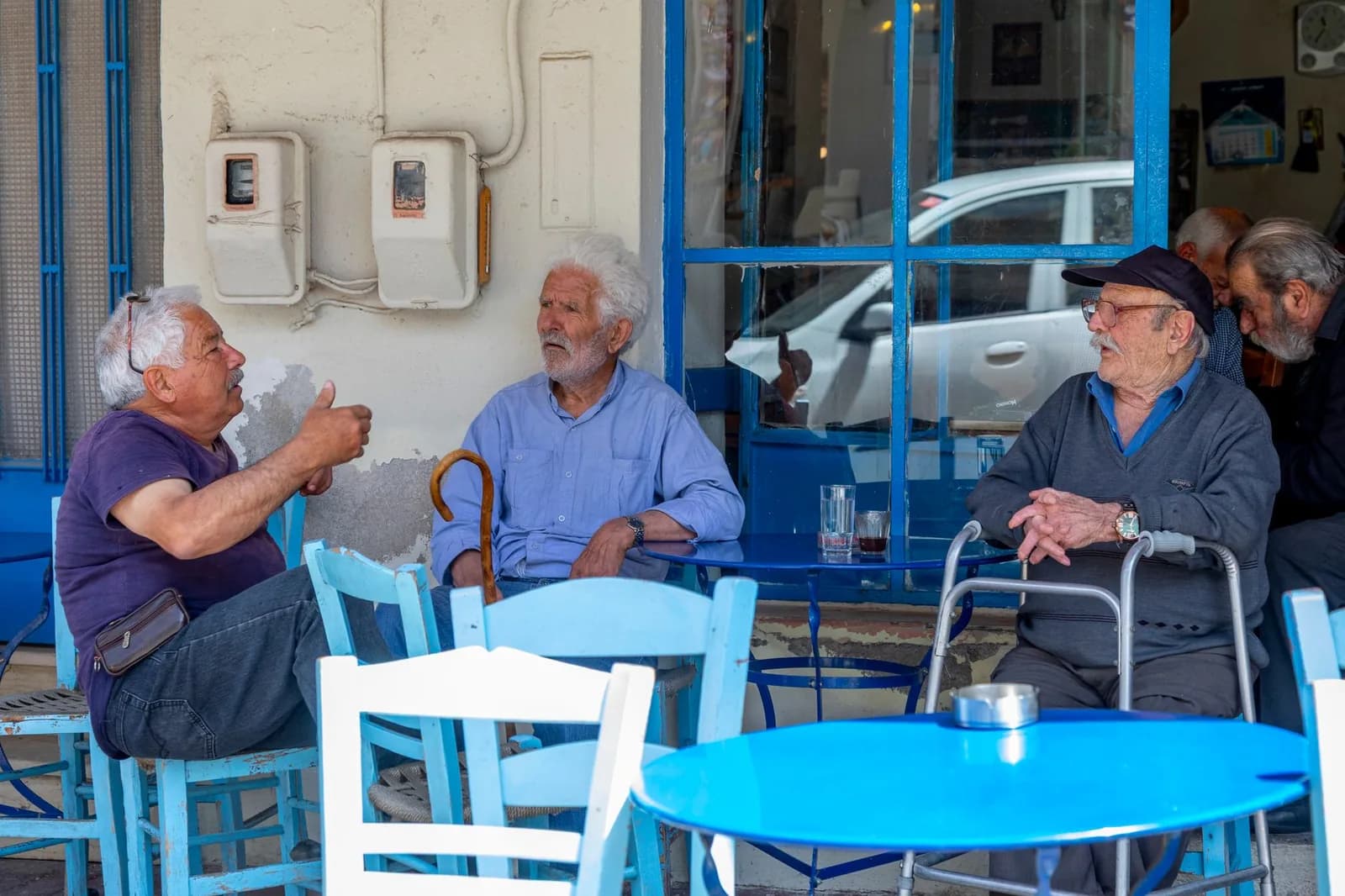 Trois hommes âgés qui discutent à la terrasse d'un café traditionnel, chaises et table bleues
