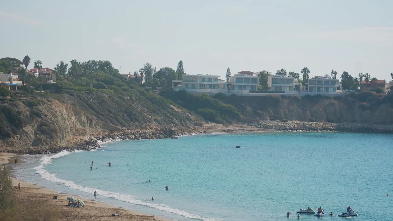 Plage de sable en croissant à Coral Bay, près de Peyia, avec baigneurs et villas au sommet des falaises