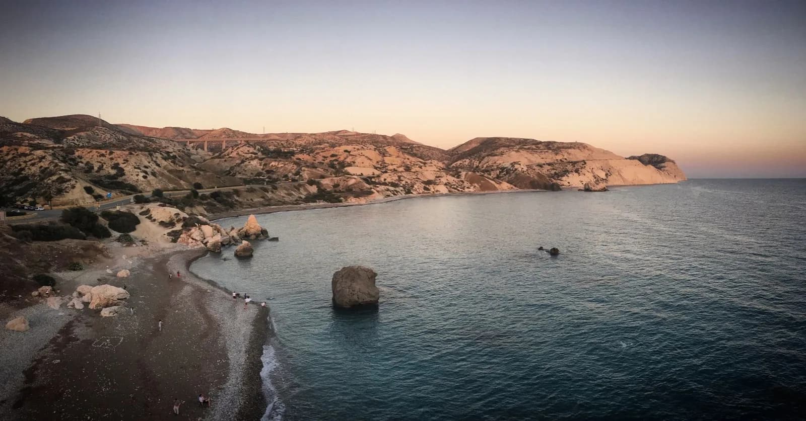 La baie de Petra tou Romiou vue d'en haut au crépuscule, avec un rocher isolé dans la mer et la côte de Paphos aux teintes orangées