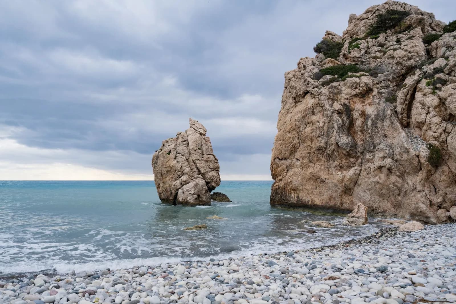 Plage de galets blancs et rocher dressé dans l'eau claire à Petra tou Romiou, près de Paphos, à Chypre, sous un ciel nuageux