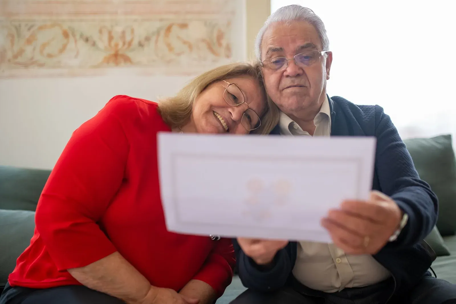 Couple de seniors sur un canapé examinant ensemble un contrat pour préparer leur épargne et sa transmission